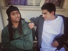 two young men sitting on a bench and one is holding a flower in his hand