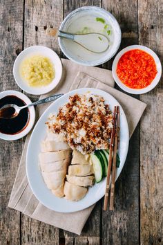 a white plate topped with meat and vegetables next to bowls of sauces on top of a wooden table