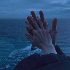 a person holding their hands up to the sky near the ocean with waves crashing in front of them