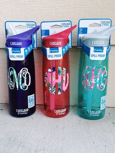 three different colored water bottles sitting next to each other on the ground in front of a wall