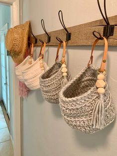 three knitted baskets hanging from hooks on a wall next to a door with a hat