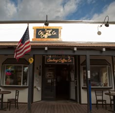 an american flag flies outside the front of a coffee shop with tables and chairs around it