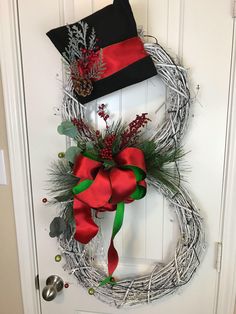 a wreath with red and green ribbons hanging on the front door next to a black hat