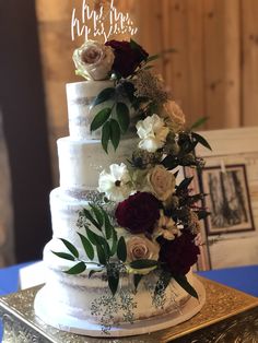 a three tiered wedding cake with white and red flowers on the top, sitting on a table