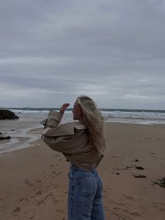 a woman standing on top of a sandy beach next to the ocean with her arms in the air