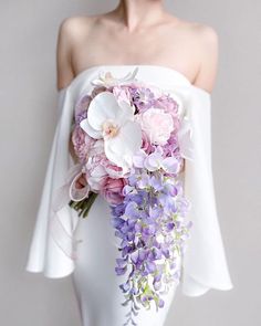 a woman wearing a white dress holding a bouquet of purple and pink flowers in her hand