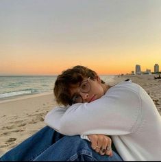 a person sitting on the beach with their arms around each other and looking at the camera