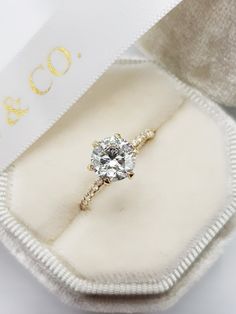 an engagement ring in a white box with gold lettering on the side and a diamond center