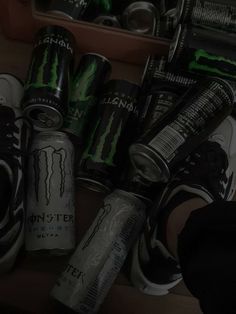 several cans and cans of monster energy drink sitting on a wooden shelf next to shoes