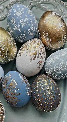 several decorated eggs sitting on top of a glass plate with gold and silver designs around them