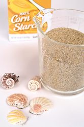 some sea shells and sand in a glass cup on a table next to a carton of corn starch