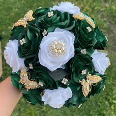 a bridal bouquet with white roses and green leaves is being held by someone's hand