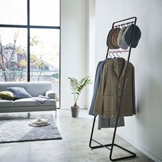 a clothes rack with hats and jackets on it in a living room next to a couch