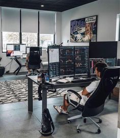 a man sitting at a desk in an office with multiple computer screens and monitors on the wall