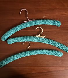 three crocheted objects are hanging on a wooden table, one is blue and the other is green