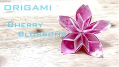 a pink origami flower sitting on top of a wooden table next to the words cherry blossoms