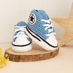 a pair of crocheted blue sneakers sitting on top of a wooden board next to yellow flowers