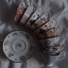 six cups and saucers are arranged on a white tablecloth, with the same pattern