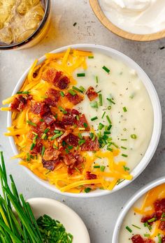 two bowls of potato soup with bacon and sour cream on the side next to green onions