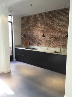 an empty kitchen with exposed brick wall in the backround and floor to ceiling windows