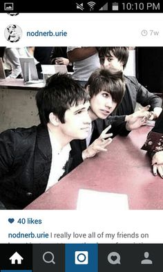 two young men sitting at a table with one pointing to the camera and another looking up