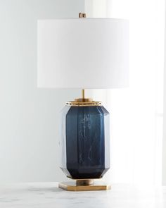 a blue glass table lamp with a white linen shade on the top and gold base