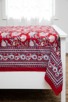 a red and blue bedspread on a white bed in front of a window