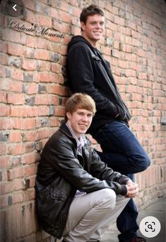 two young men leaning against a brick wall