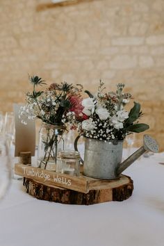 flowers are in a watering can on top of a wooden slice at the head table