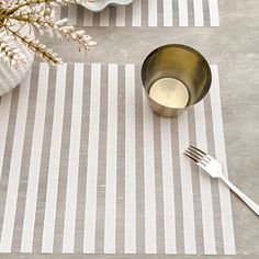 a place setting with silverware and flowers on a striped tablecloth next to a bowl