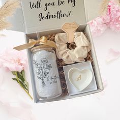 an open box containing two personal items and a heart shaped dish in front of pink flowers