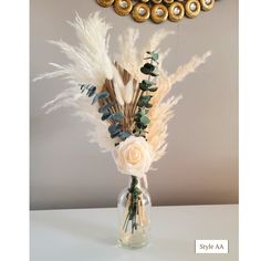 a vase filled with white flowers and feathers on top of a table next to a clock