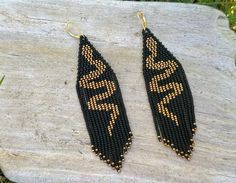 two black and gold beaded earrings sitting on top of a piece of wood next to grass