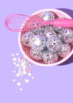 a pink whisk is in a bowl filled with disco balls and star shaped confetti