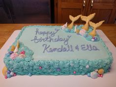 a birthday cake with blue frosting and mermaid decorations on it's side, sitting on a table