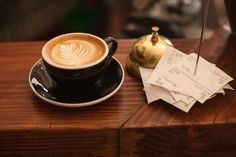 a cappuccino on a saucer next to a stack of tickets and a golden teapot