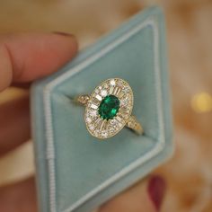 a close up of a person's hand holding a ring with a green stone in it