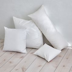 four white pillows sitting on top of a wooden floor next to a lamp and vase