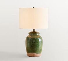 a green ceramic table lamp with a white shade on the base and a beige linen lampshade