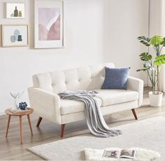 a living room with a white couch and two tables in front of the window, along with pictures on the wall