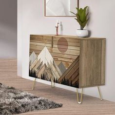 a wooden cabinet with mountains and trees painted on the side by metal legs in front of a white wall