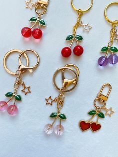 four different key chains with cherries and charms attached to them on a white surface