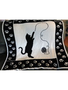 a black and white blanket with a cat holding a ball of yarn in it's paws