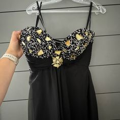 a woman's hand holding up a black and gold dress on a hanger