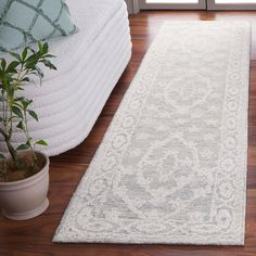 a large white rug on top of a hard wood floor next to a potted plant