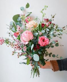 a person holding a bouquet of flowers in their hand with greenery on the side