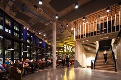 people are sitting at tables in a large room with stairs and lights hanging from the ceiling