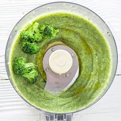 broccoli and pesto in a food processor with a white lid on a wooden table