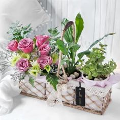 a basket filled with pink roses and greenery on top of a white tablecloth