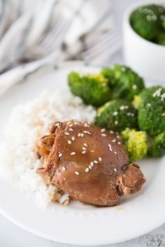 a white plate topped with meat and rice next to broccoli on a table